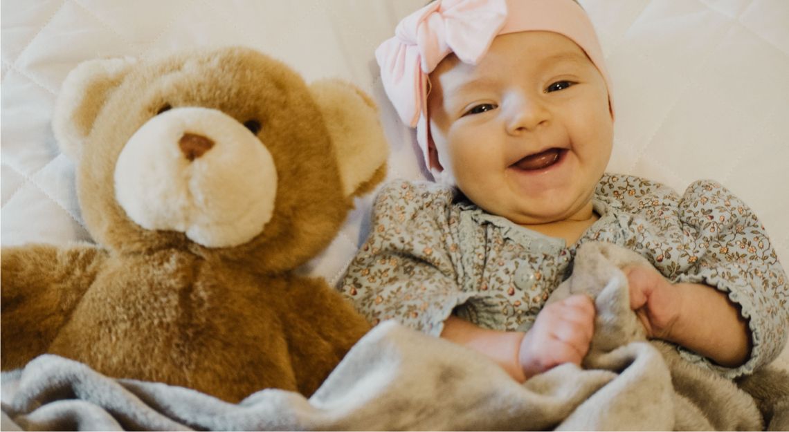 Un enfant souriant bordé de son ours en peluche
